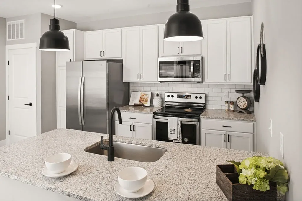 Modern Columbus apartment kitchen featuring stainless steel appliances, white cabinets, and granite countertops. Two black pendant lights hang above a central island with a sink and two pristine white bowls.