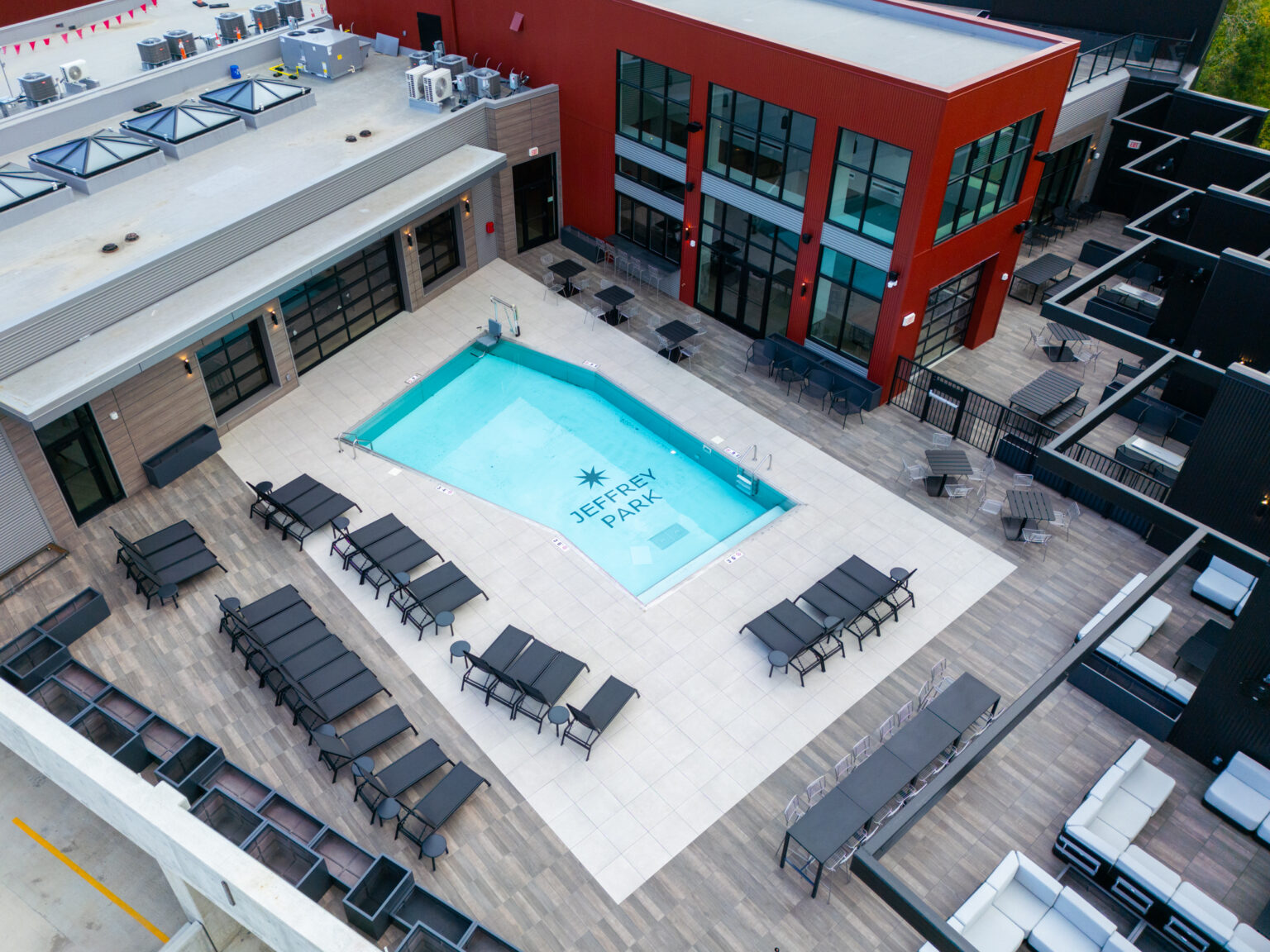 Aerial view of a modern outdoor pool area at Columbus apartments, with Jeffrey Park elegantly inscribed on the pool floor, surrounded by sleek lounge chairs and a striking red building.