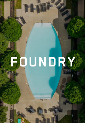 Aerial view of an outdoor swimming pool surrounded by lounge chairs and trees at Columbus apartments, with the word FOUNDRY centered over the pool.