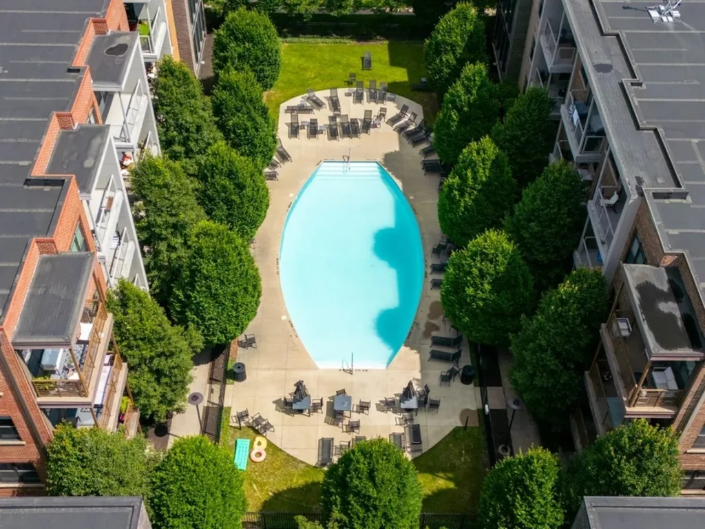Aerial view of a residential courtyard featuring a central swimming pool surrounded by trees and lounge chairs, with apartment buildings on each side.