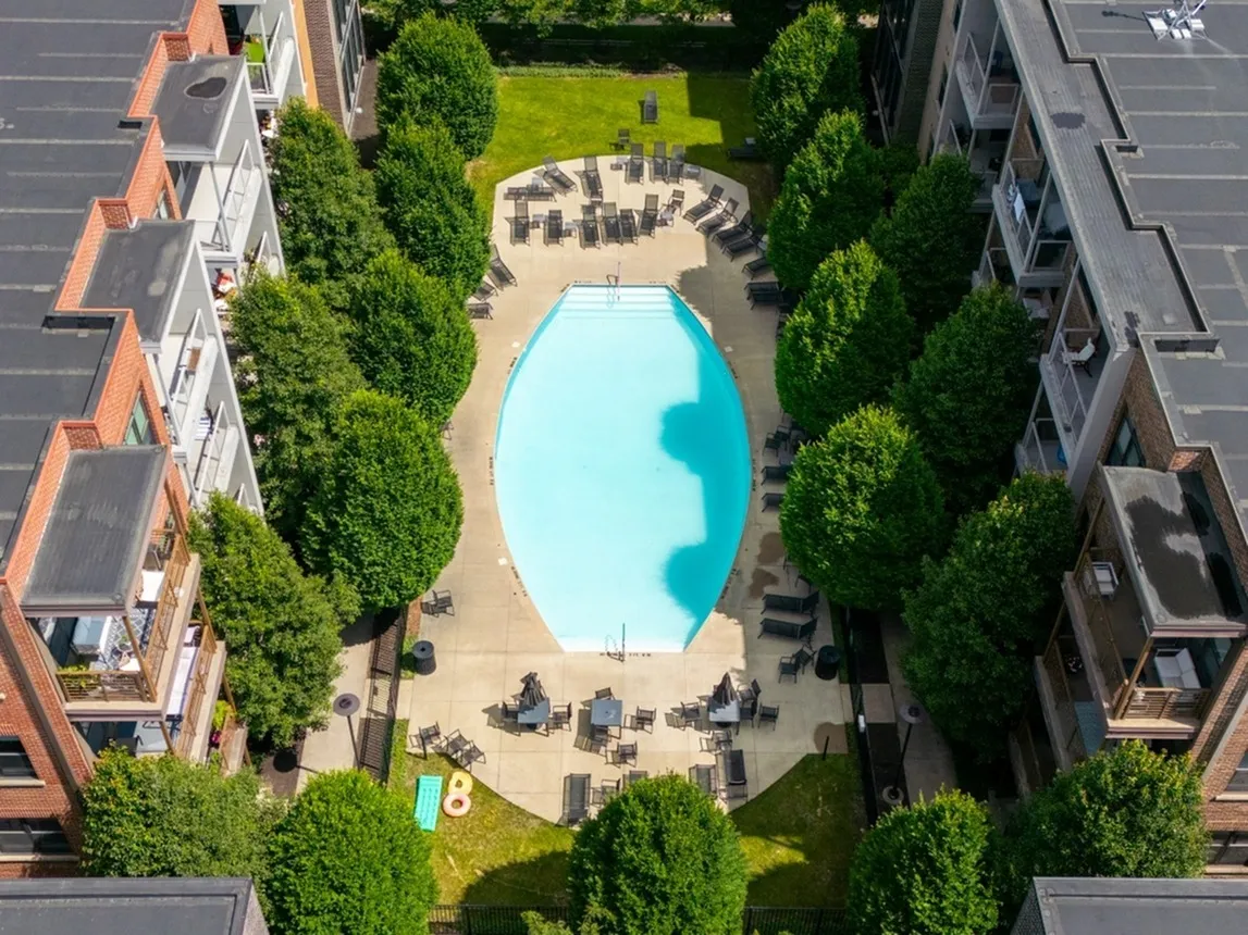Aerial view of a residential courtyard featuring a central swimming pool surrounded by trees and lounge chairs, with apartment buildings on each side.