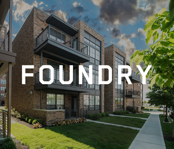 Columbuss modern brick apartment building, FOUNDRY, features balconies and is embraced by sidewalks and lush greenery.