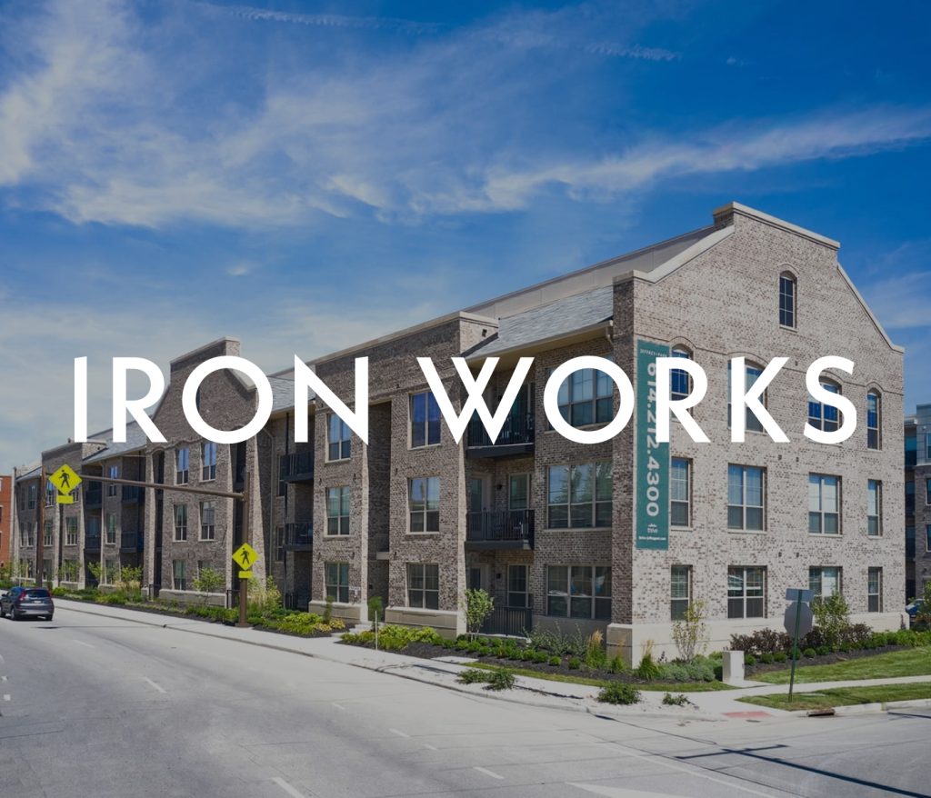 A street view of Iron Works, a charming brick building with three stories and balconies, nestled under a clear blue sky, showcasing the essence of Columbus apartments.