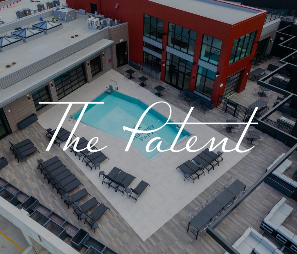 Rooftop view of The Patent building at Columbus Apartments, featuring a central swimming pool surrounded by lounge chairs and seating areas. This modern structure boasts striking red and gray accents, offering a chic urban retreat.