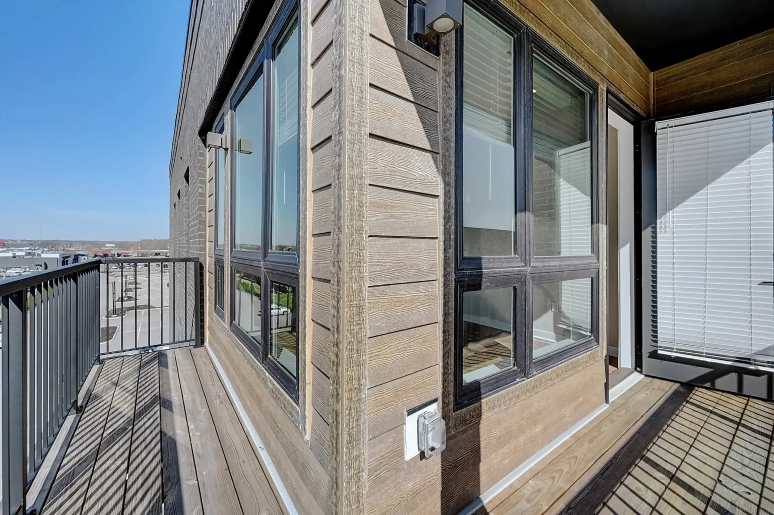 Corner view of a modern wooden balcony in the exquisite Columbus apartments, featuring large windows, a sleek railing, and a clear blue sky in the background.