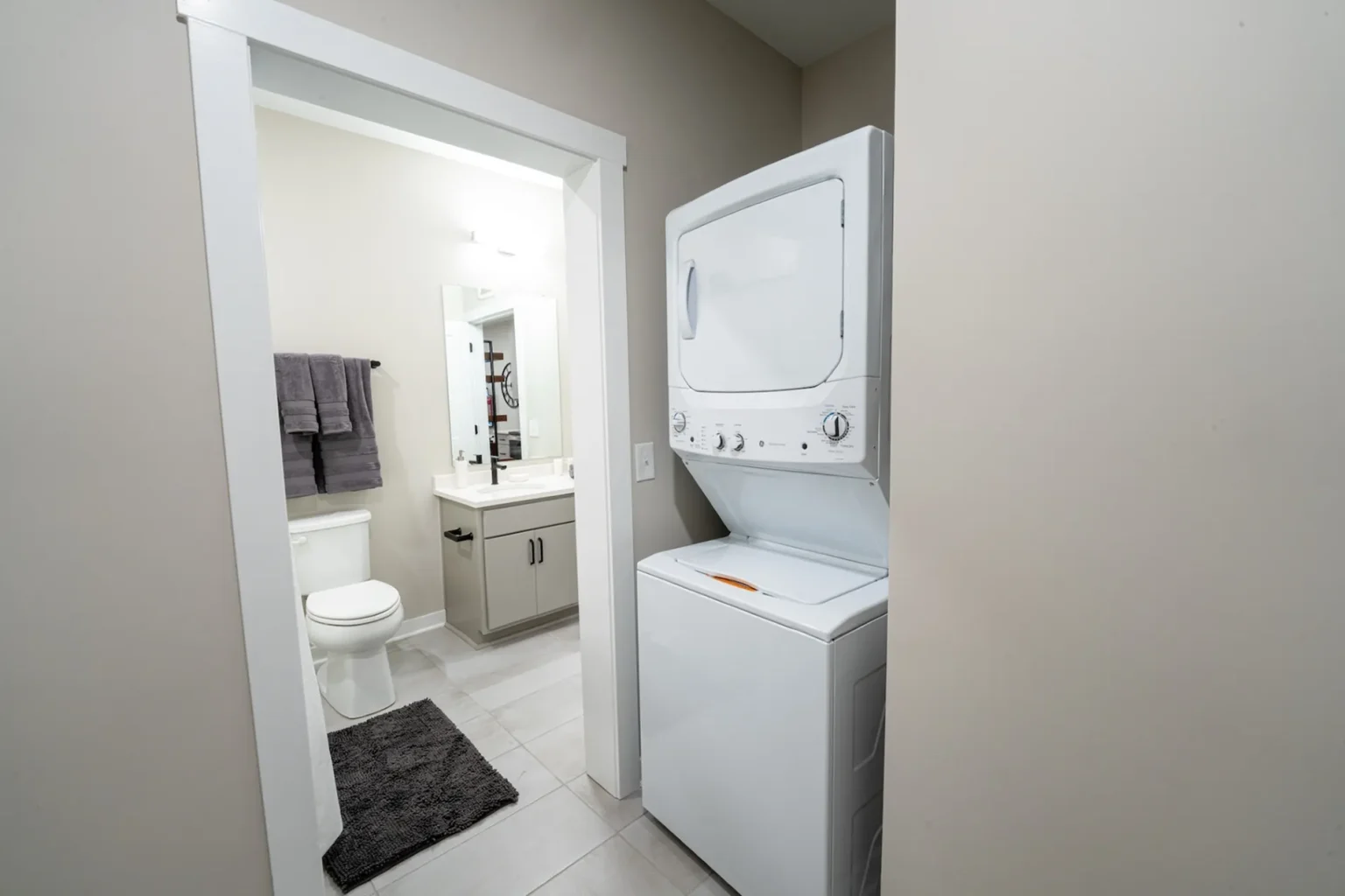Compact laundry area with a stacked washer and dryer next to a bathroom in Columbus apartments. The bathroom includes a toilet, sink, mirror, and towel rack.