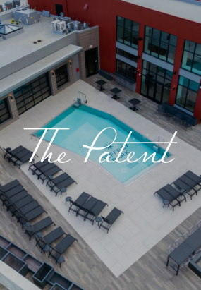 Aerial view of a modern outdoor pool area with lounge chairs and tables, surrounded by a red building at The Patent at Jeffrey Park. The words The Patent are overlaid on the image.