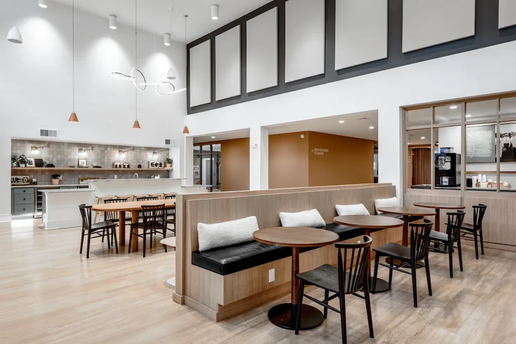 A modern cafe interior with wooden tables, black chairs, and bench seating mirrors the sleek style of Columbus apartments. Overhead lighting and natural wood flooring enhance the clean, contemporary design.