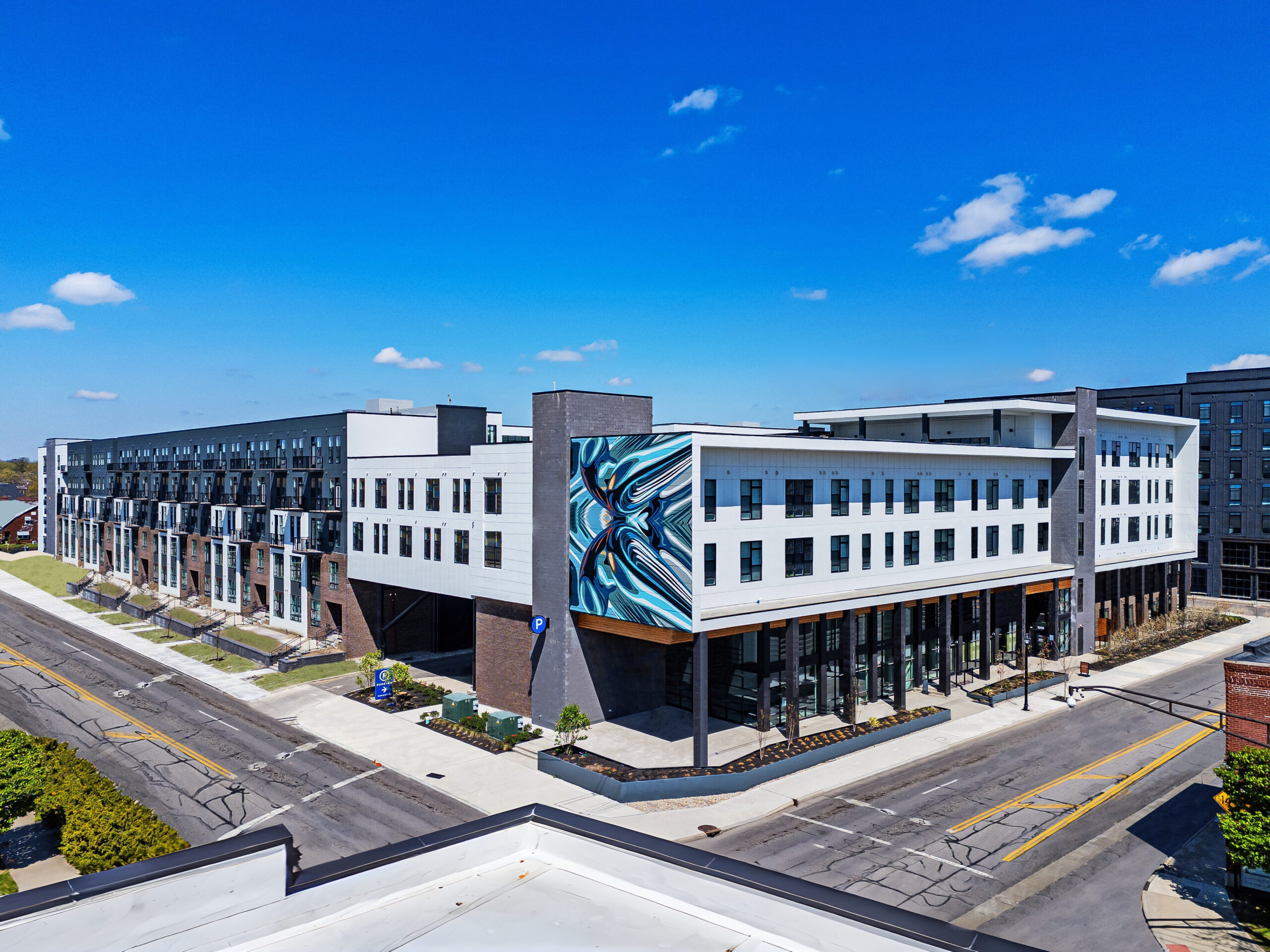 4th and 5th Modern Columbus apartments complex featuring a striking mural on the corner, large windows, and street-level retail under a clear blue sky.