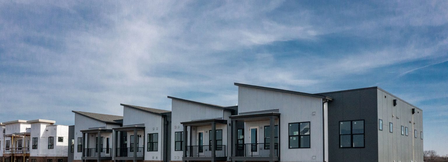 Row of modern, minimalist townhouses with flat roofs and large windows under a partly cloudy sky.