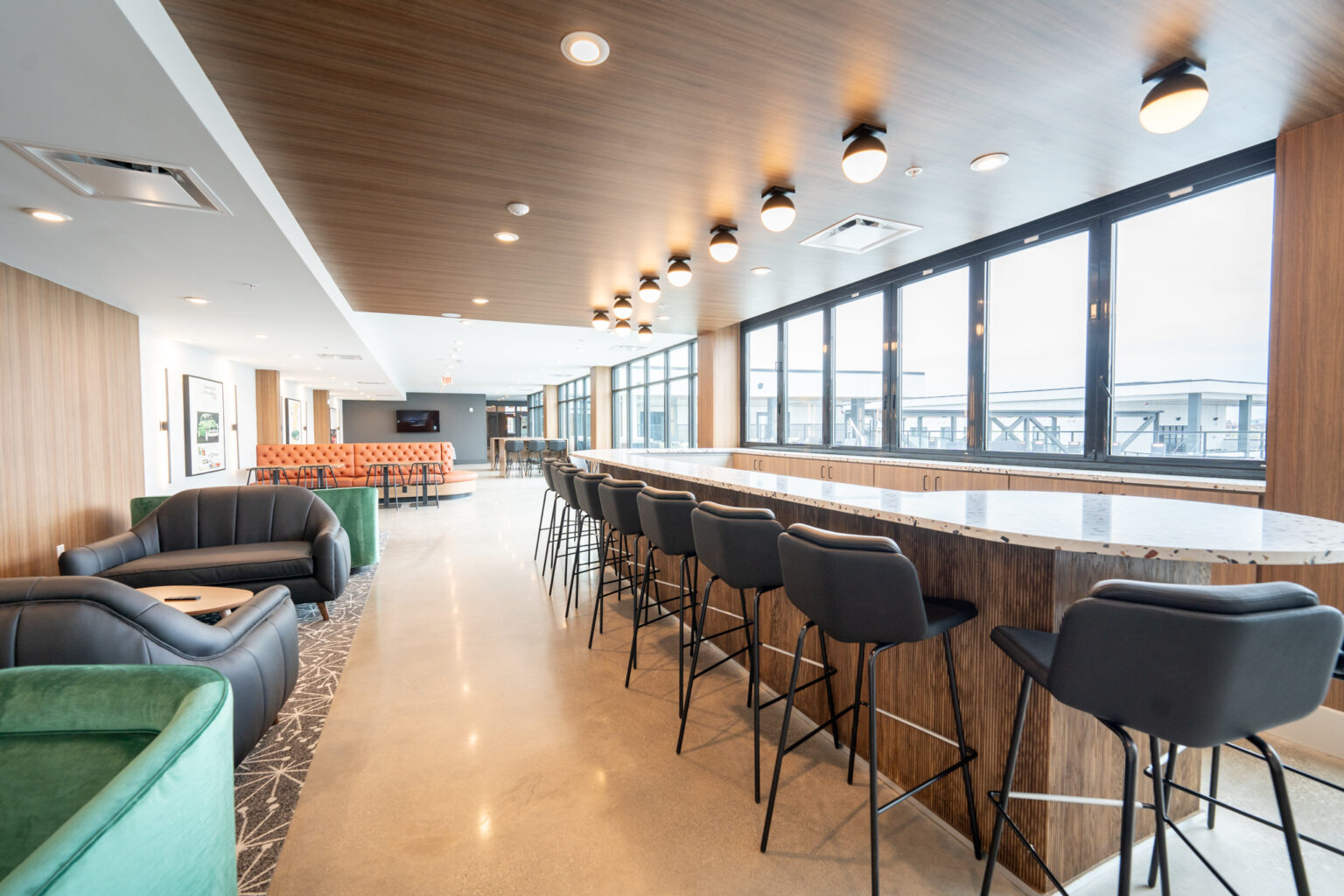 Thrive Companies, Modern lounge area with bar seating, marble countertop, green and black chairs, large windows, and wood-paneled ceiling. Enjoy natural light in this spacious, contemporary room at 4th and 5th Apartments Columbus Ohio. Apartments in Columbus Ohio