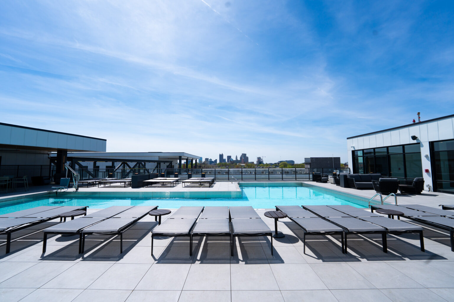 Rooftop swimming pool area with lounge chairs under a clear blue sky, city skyline visible in the distance—experience elevated living at Columbus apartments.