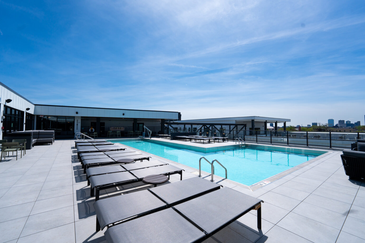 Rooftop swimming pool with lounge chairs and seating areas, under a clear blue sky, offers stunning city skyline views from Columbus apartments.