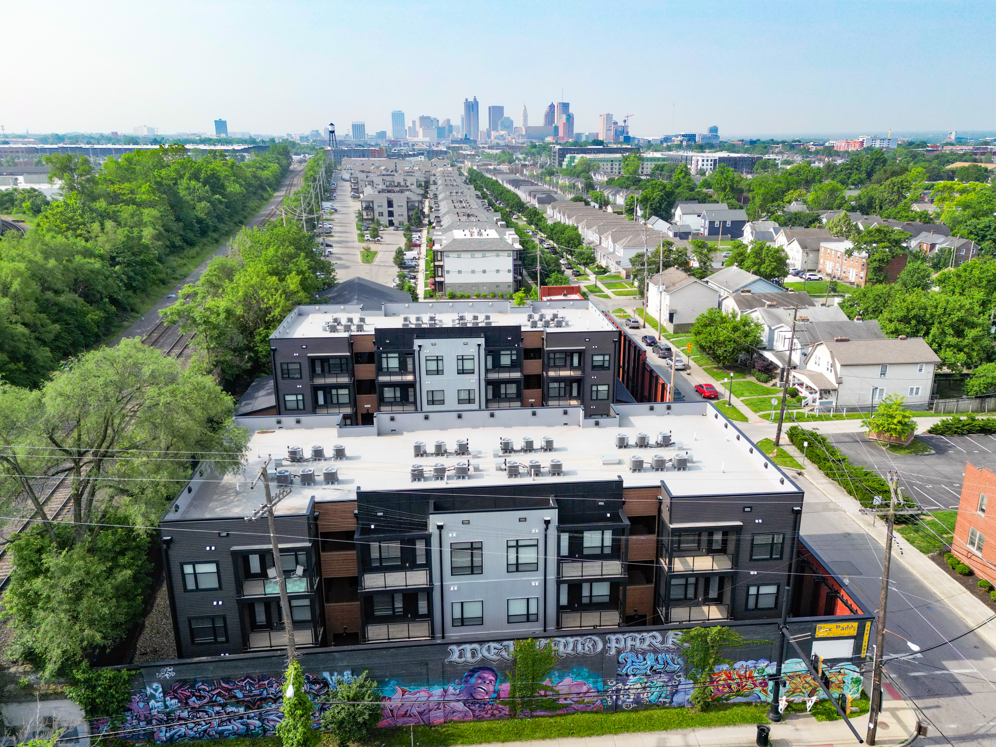 Aerial view of Columbus apartments 1460 Grant featuring rooftop seating, vibrant street art on the front wall, and a distant city skyline in the background on a clear day.