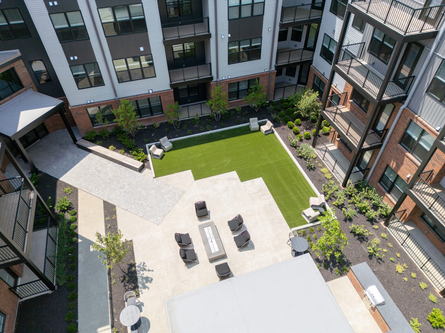Aerial view of Trace Quarter’s modern apartment courtyard featuring artificial grass, seating areas, fire pit, and landscaped plants.