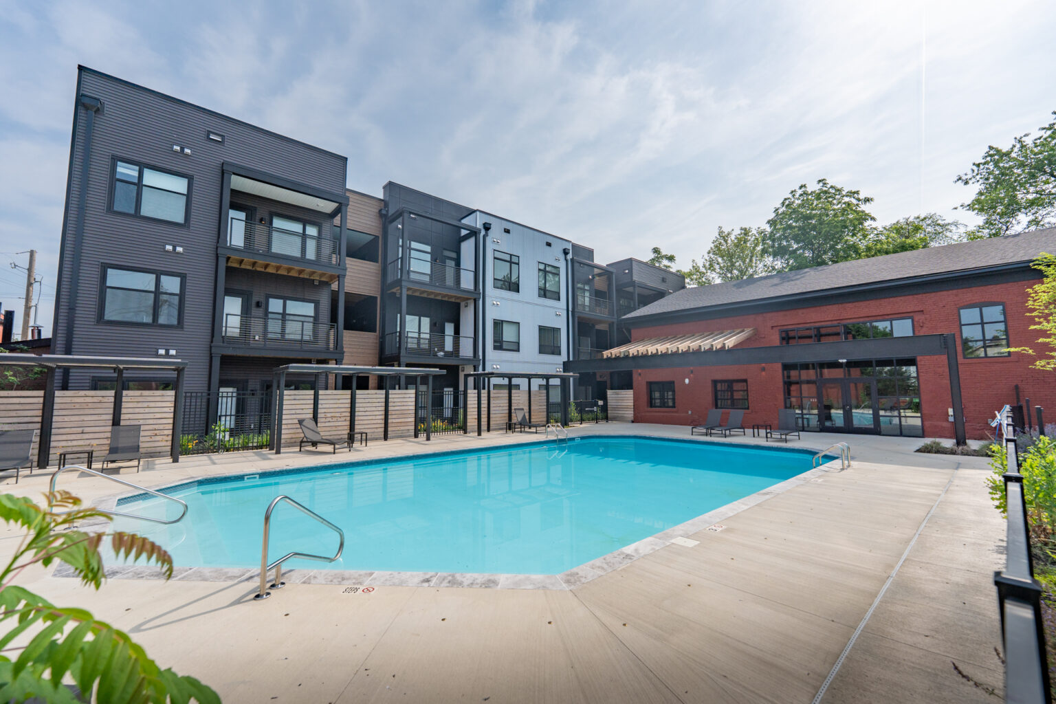 1460 Grant Outdoor swimming pool surrounded by a concrete deck, adjacent to modern Columbus apartments and a red brick building, under a partly cloudy sky.