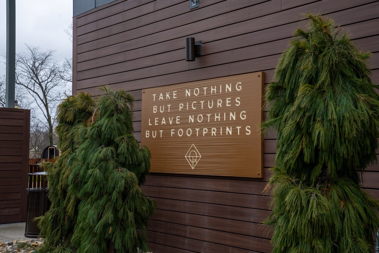 A wooden wall adorned with a sign that reads, Take nothing but pictures, leave nothing but footprints, stands beside the vibrant green foliage, echoing the harmonious ethos often found near serene Columbus apartments.