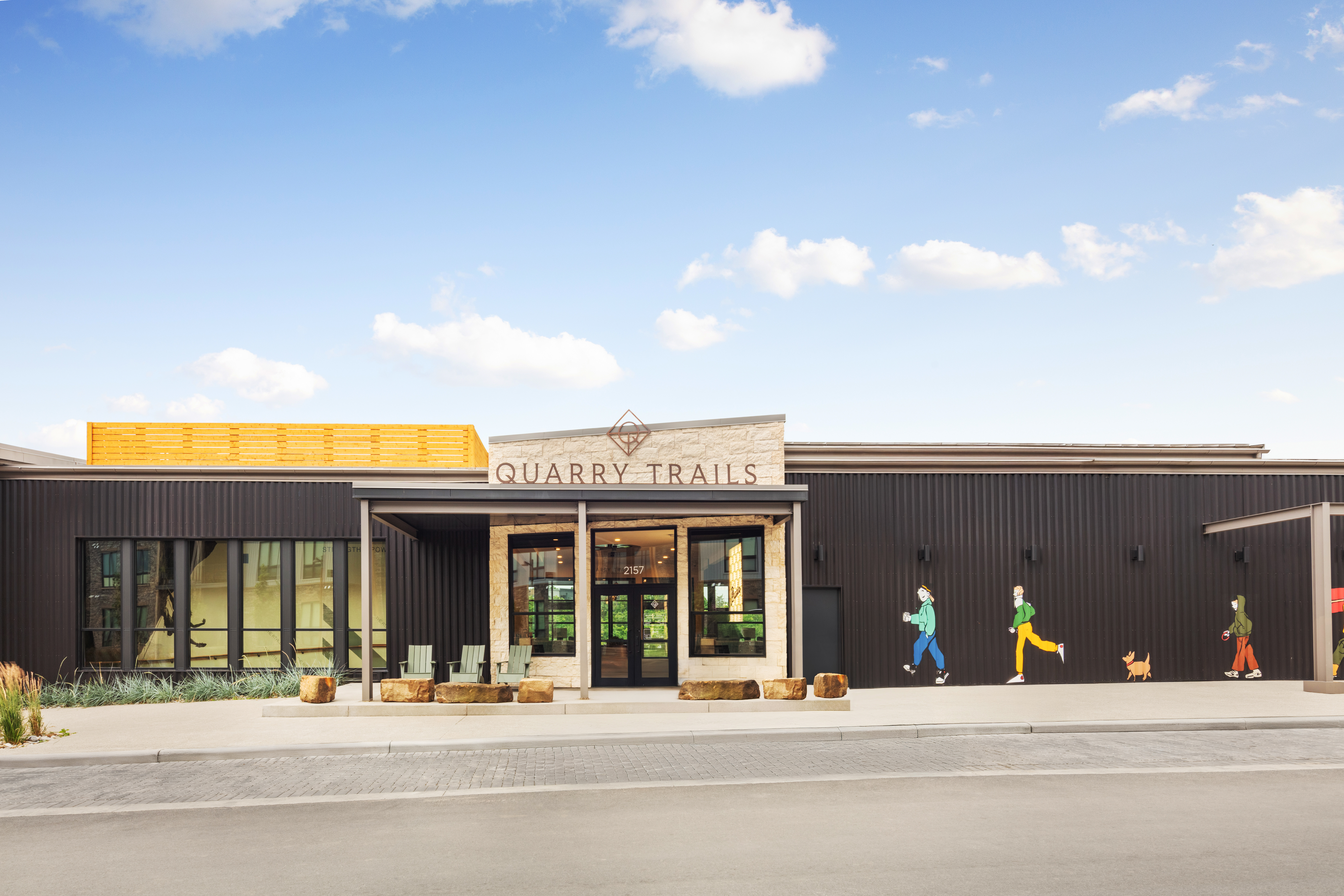 A modern building with a sign reading Quarry Trails above the entrance; colorful murals of people and a dog are painted on the black exterior wall, making these Columbus apartments stand out with vibrant urban charm.