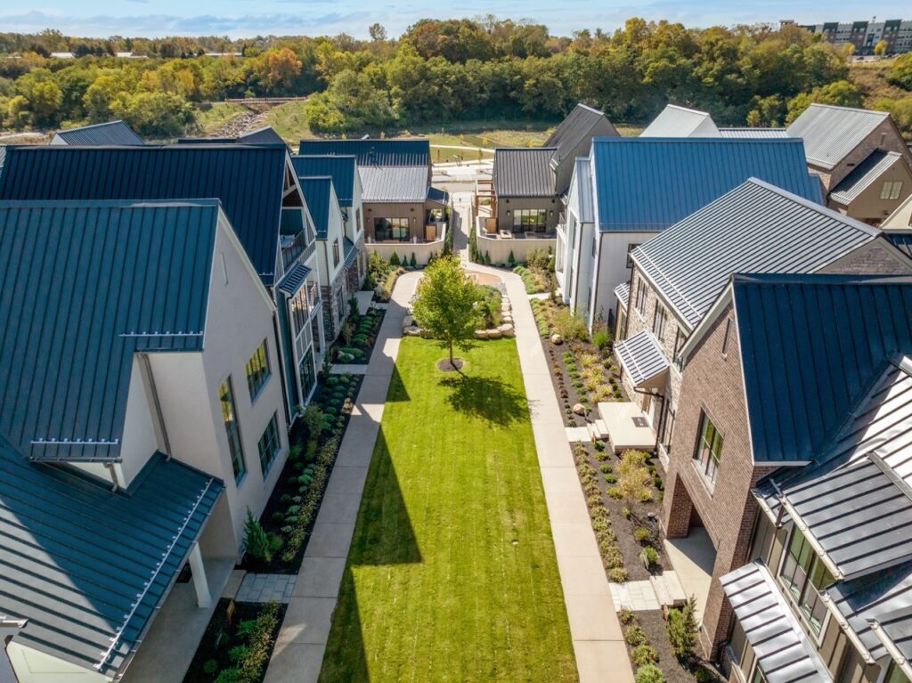 Aerial view of Columbus apartments showcasing modern houses with metal roofs, a central green lawn, and surrounding trees in the background.