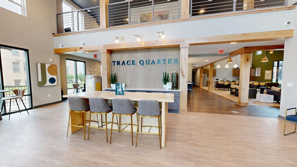 Modern Trace Quarter lobby with a wooden counter, four chairs, and TRACE QUARTER sign on the wall; open, well-lit space featuring upstairs railing and seating areas.