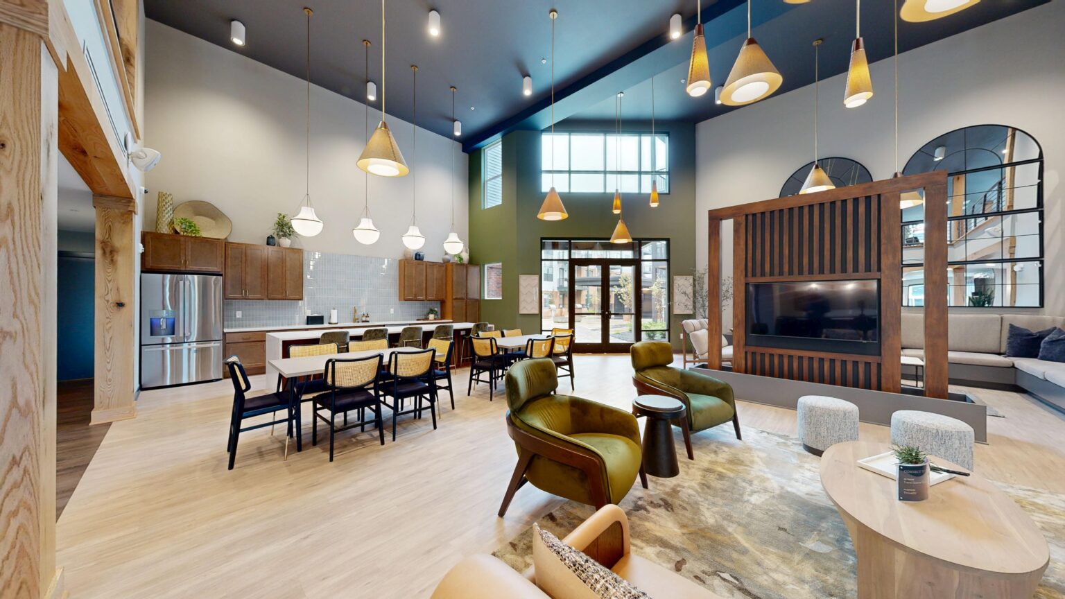 Modern open-concept Trace Quarter lounge with high ceilings, a kitchen area, dining table, various seating, pendant lights, and large windows letting in natural light.