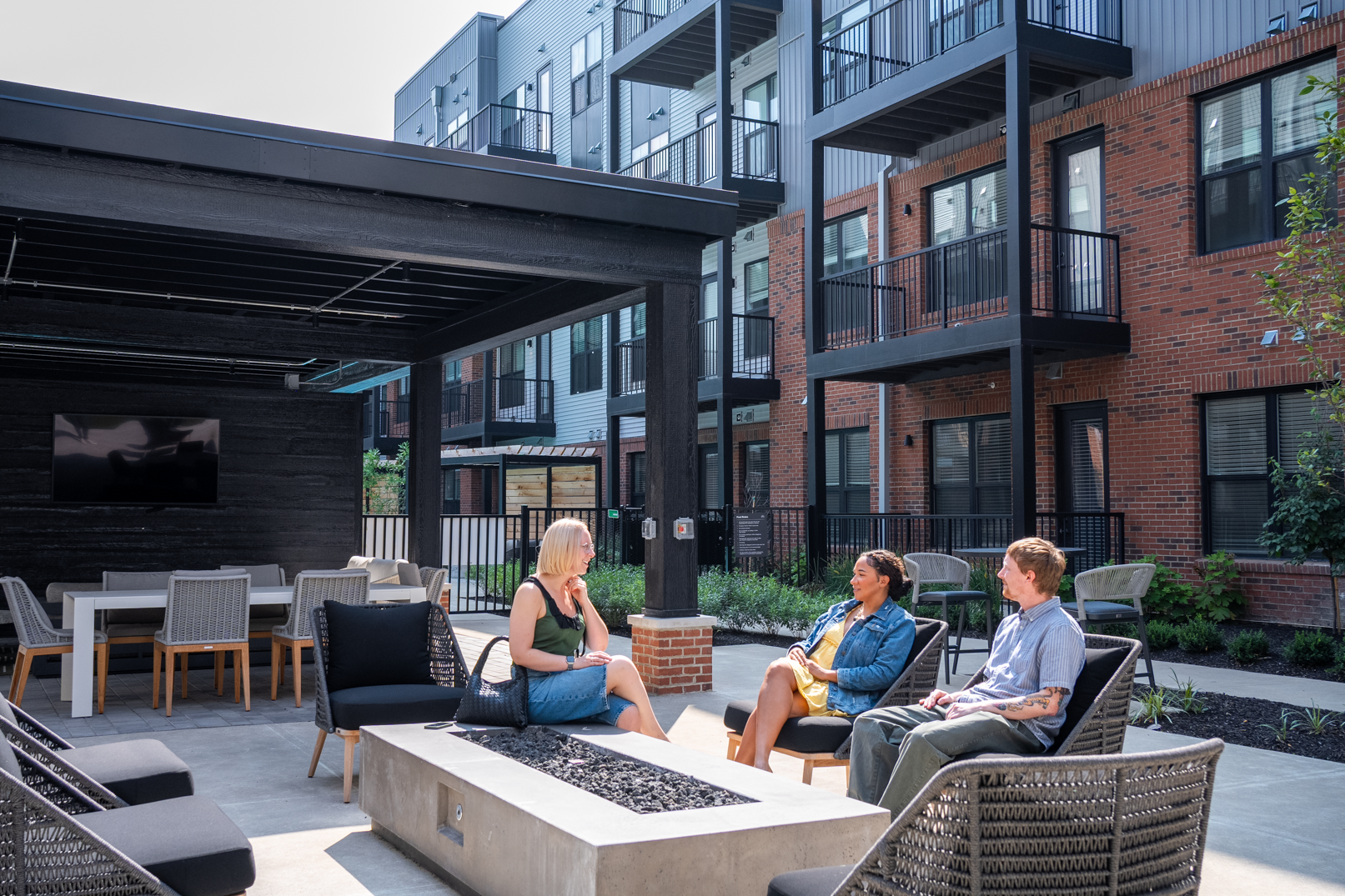 Three people sit and talk around a fire pit at Trace Quarter, enjoying the modern outdoor patio area of the apartment complex on a sunny day.