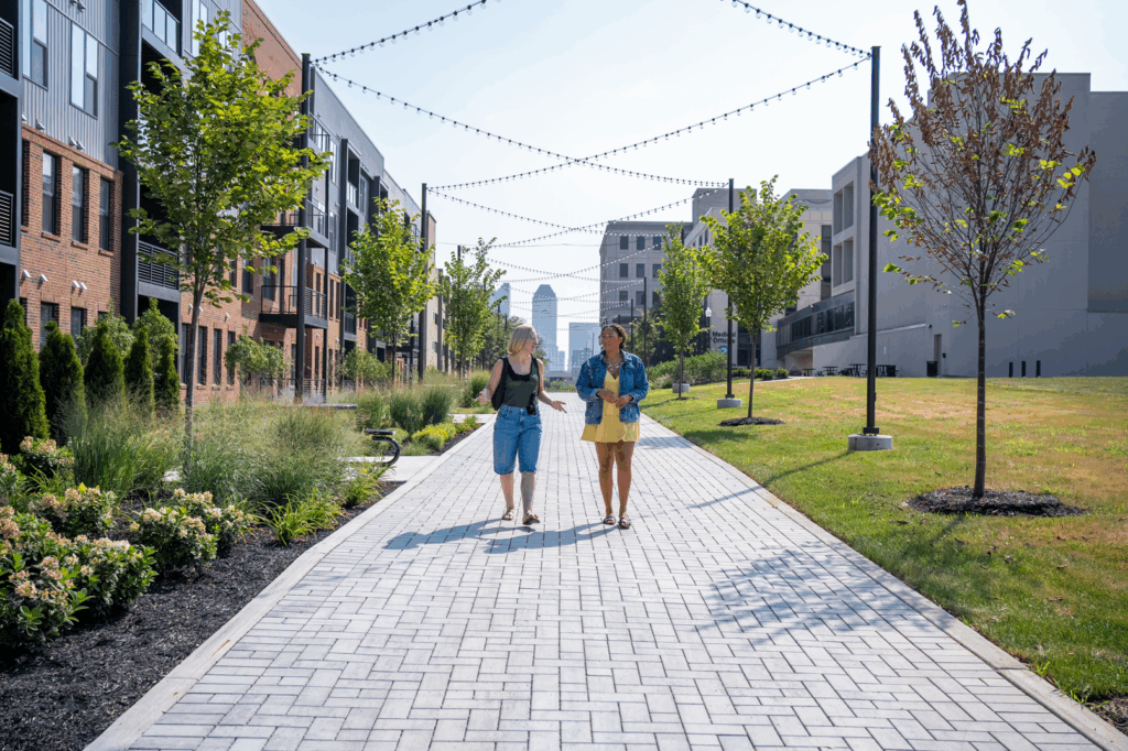 Tree-lined walking path with string lights at Trace Quarter, with Downtown Columbus in the distance