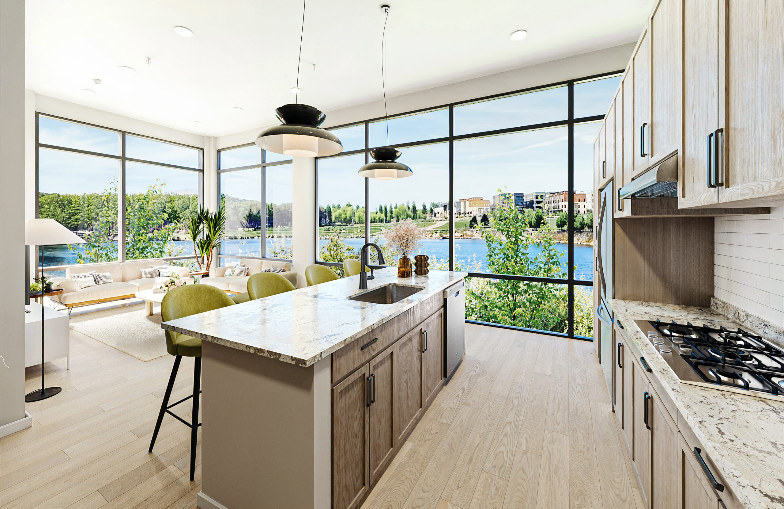 South Bank West Modern open-concept kitchen with an island, gas stove, and large windows overlooking a river and cityscape at South Bank at Quarry Trails, adjacent to a bright living area.