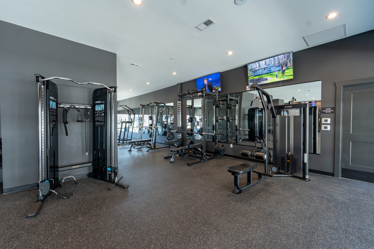 Modern gym with black exercise machines, benches, large mirrors, wall-mounted TVs, and gray walls, featuring a clean and organized layout.