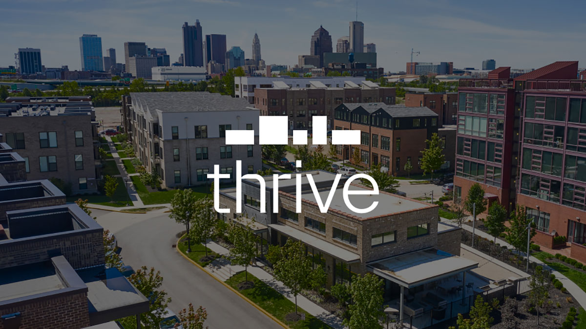 Aerial view of a modern urban neighborhood with several buildings and a distant city skyline. The word thrive is prominently displayed in the center.