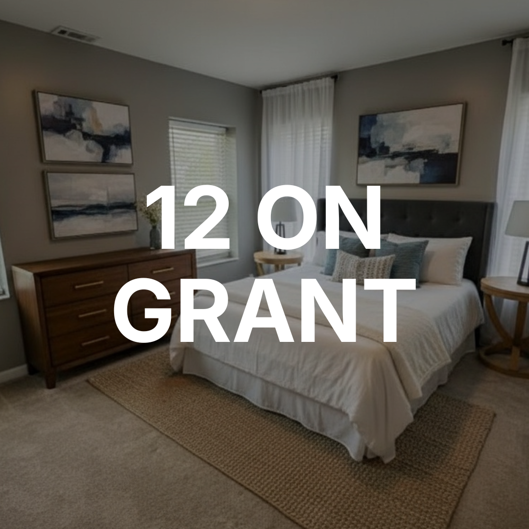 Thrive Companies, A modern bedroom with a bed, wooden dresser, round side table, two paintings, and large text overlay that reads 12 ON GRANT. Apartments in Columbus Ohio