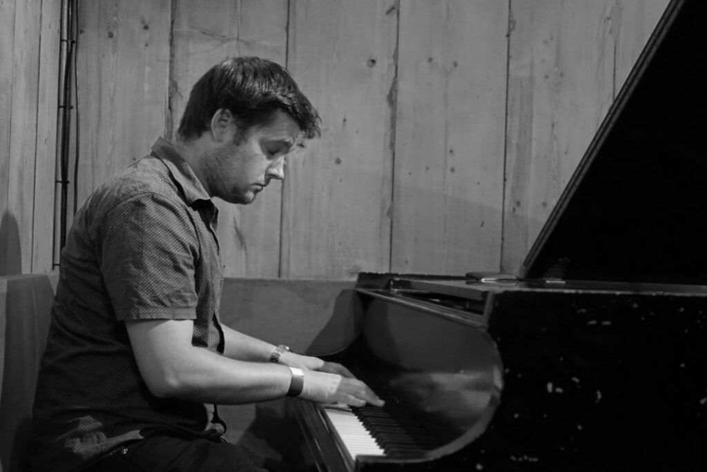 Thrive Companies, A man sits at a grand piano, playing with concentration. The background consists of wooden panels. The image is in black and white. Apartments in Columbus Ohio