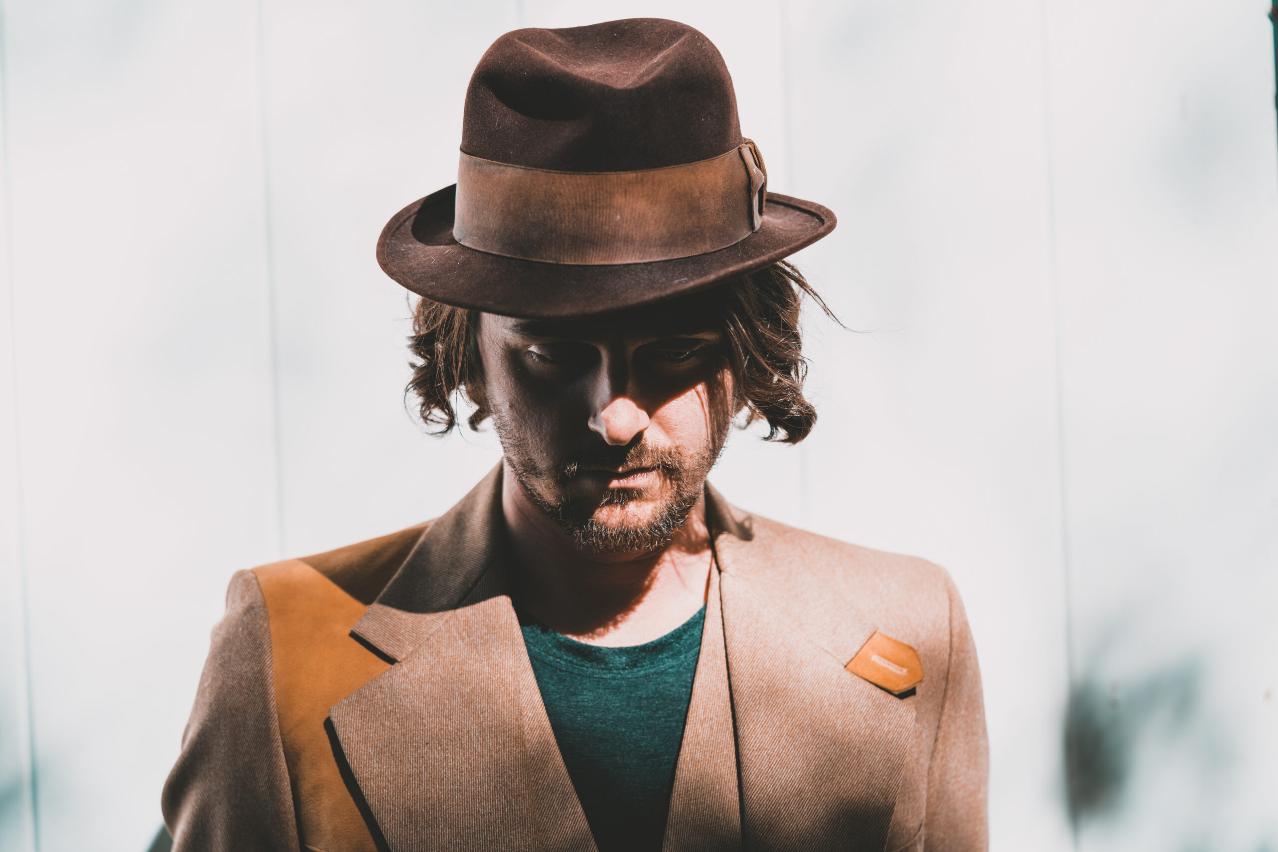 Thrive Companies, Man wearing a brown fedora and tan blazer stands in partial shadow against a light background. Apartments in Columbus Ohio