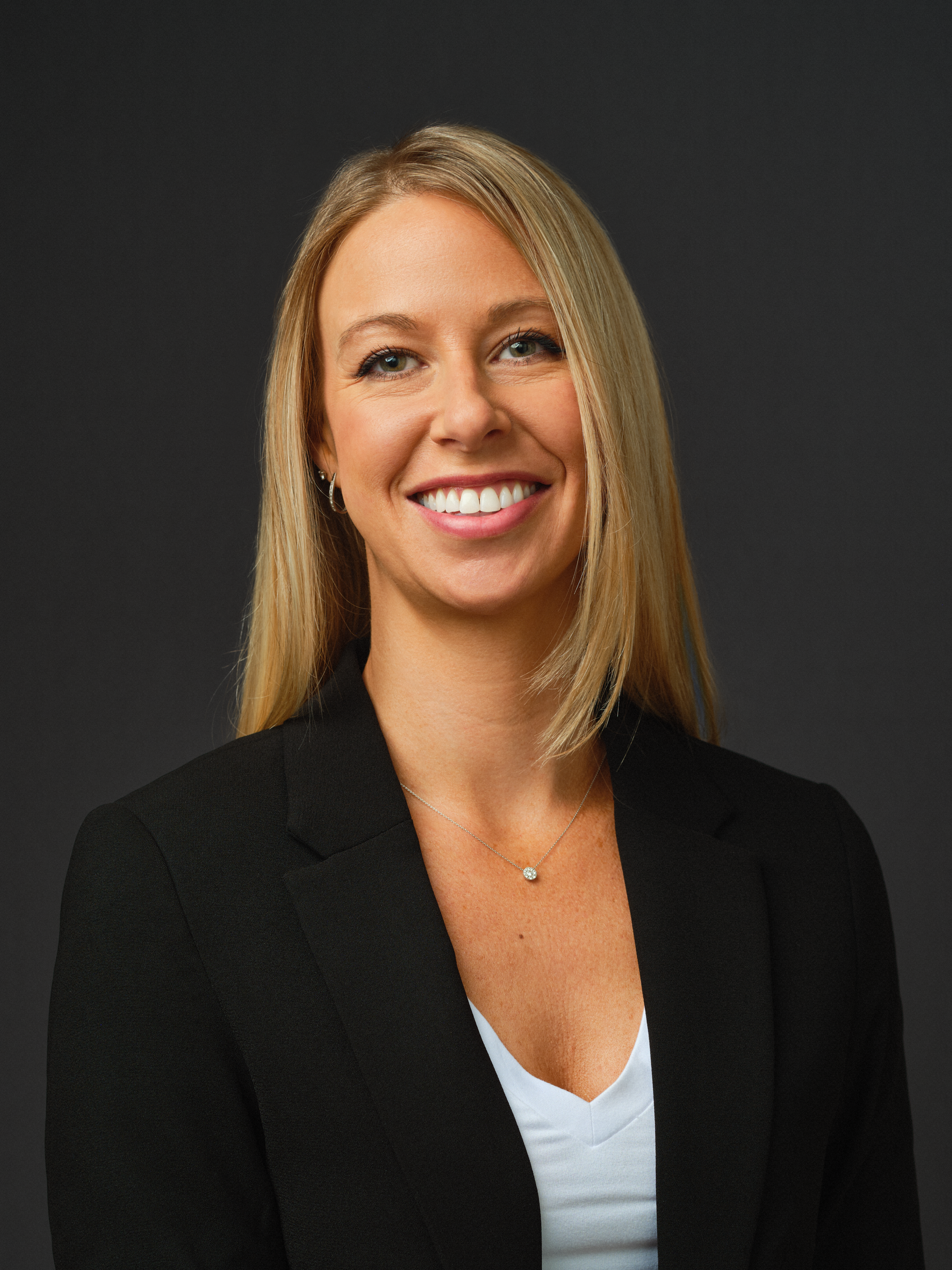Thrive Companies, A woman with straight blonde hair, wearing a black blazer over a white top, smiles in front of a plain dark background. Apartments in Columbus Ohio