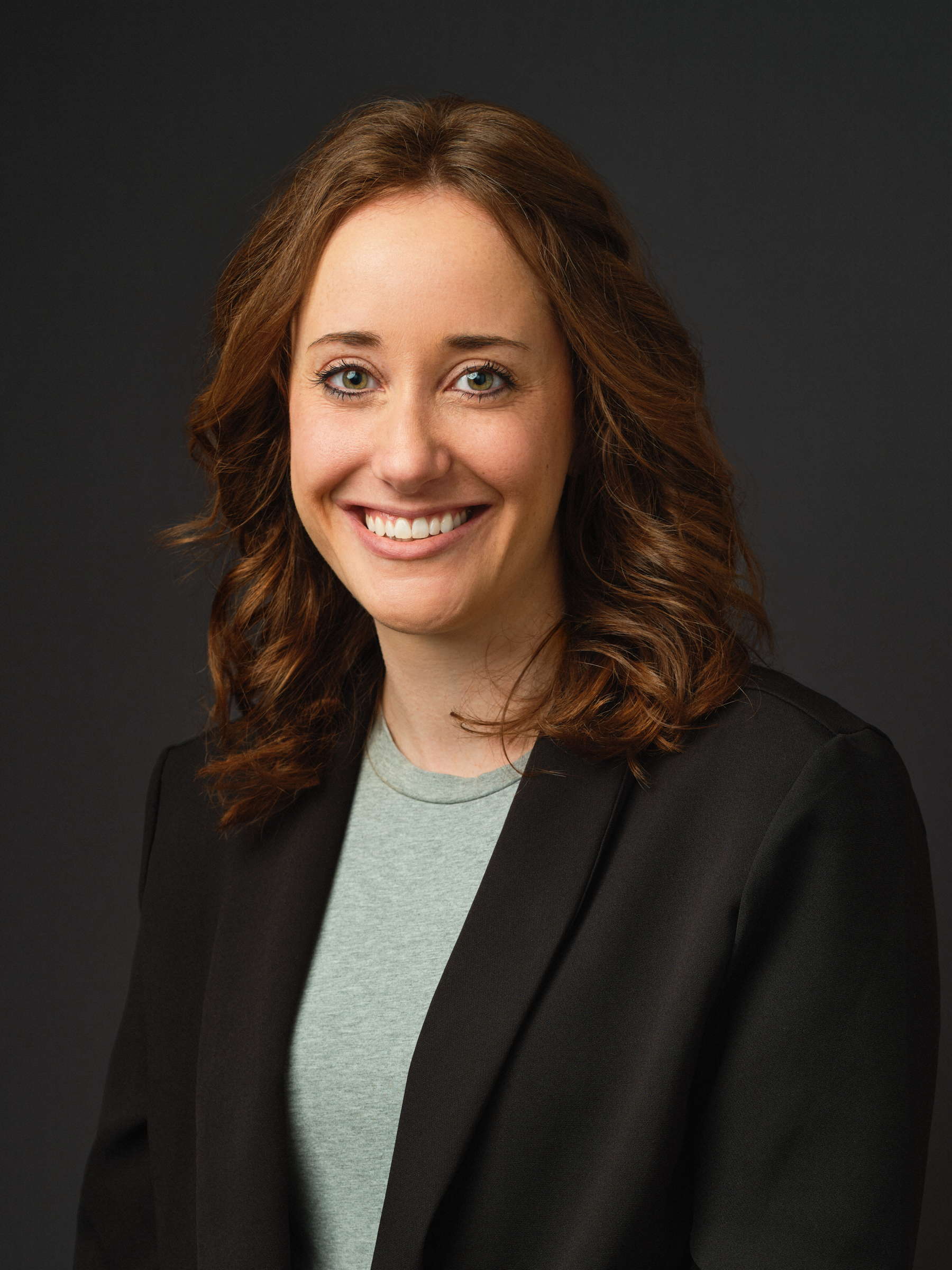 Thrive Companies, A woman with shoulder-length brown hair, wearing a black blazer over a gray shirt, smiles at the camera against a plain dark background. Apartments in Columbus Ohio