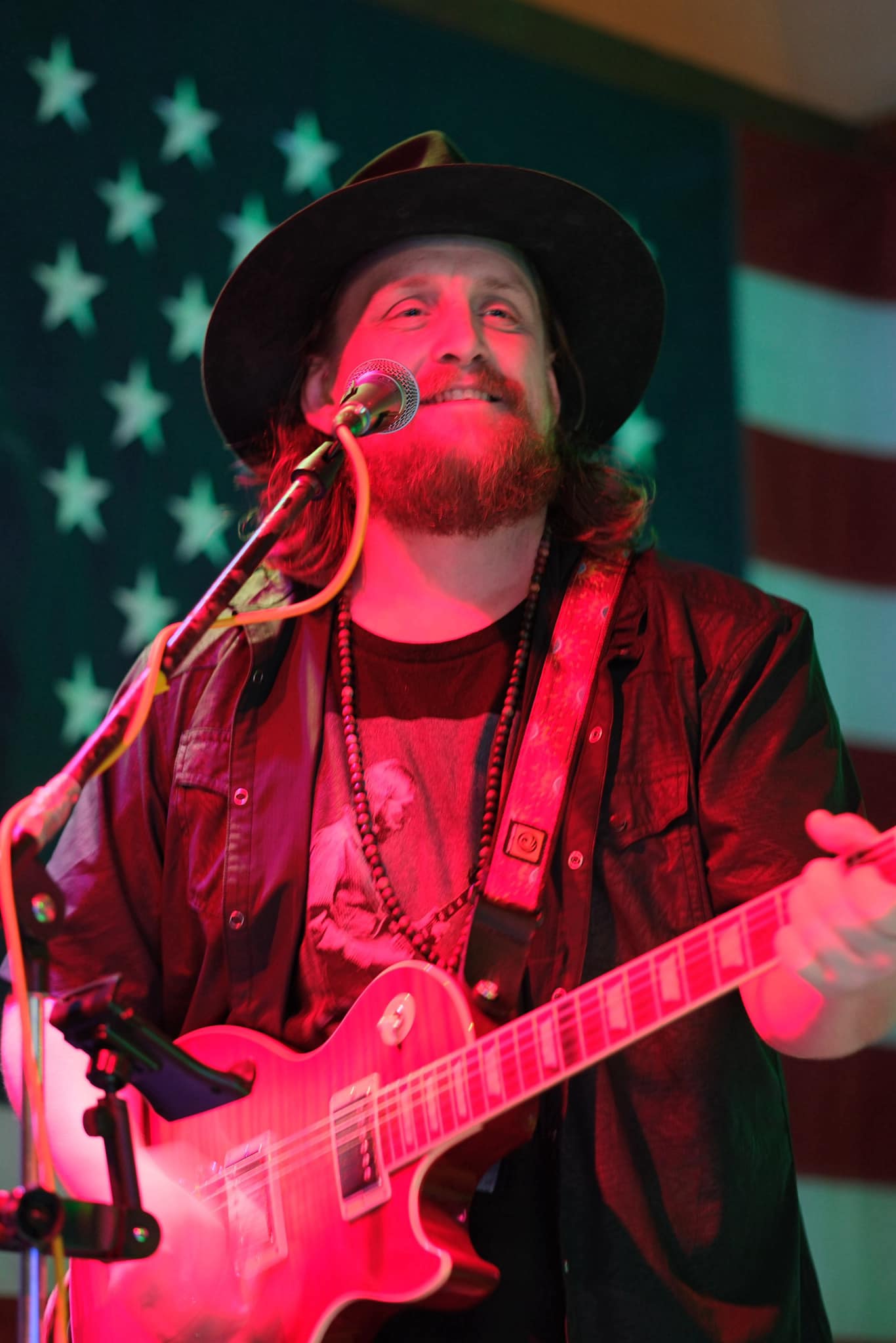 Thrive Companies, A man with a beard and long hair plays an electric guitar and sings into a microphone, standing in front of an American flag. Apartments in Columbus Ohio