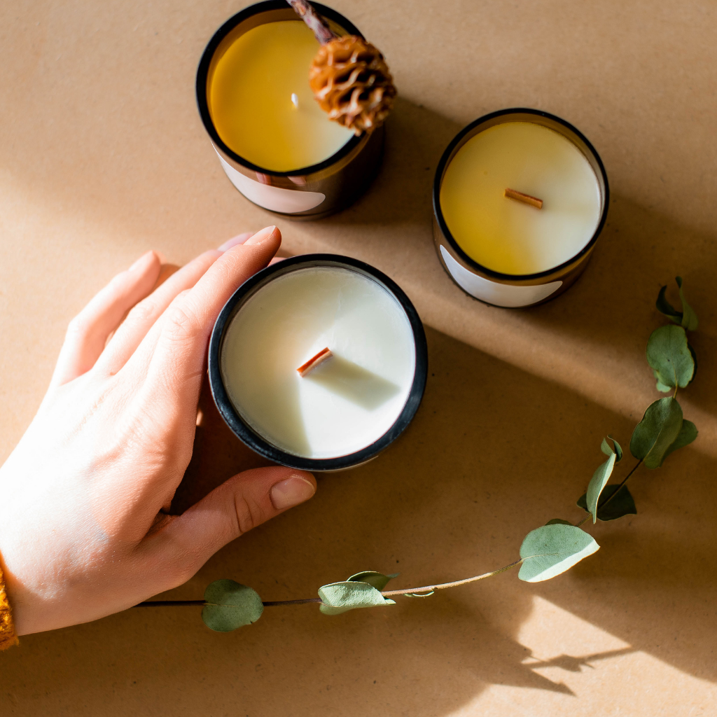 Thrive Companies, A hand reaches for one of three candles in glass jars on a brown surface, with eucalyptus leaves and a pinecone nearby. Apartments in Columbus Ohio