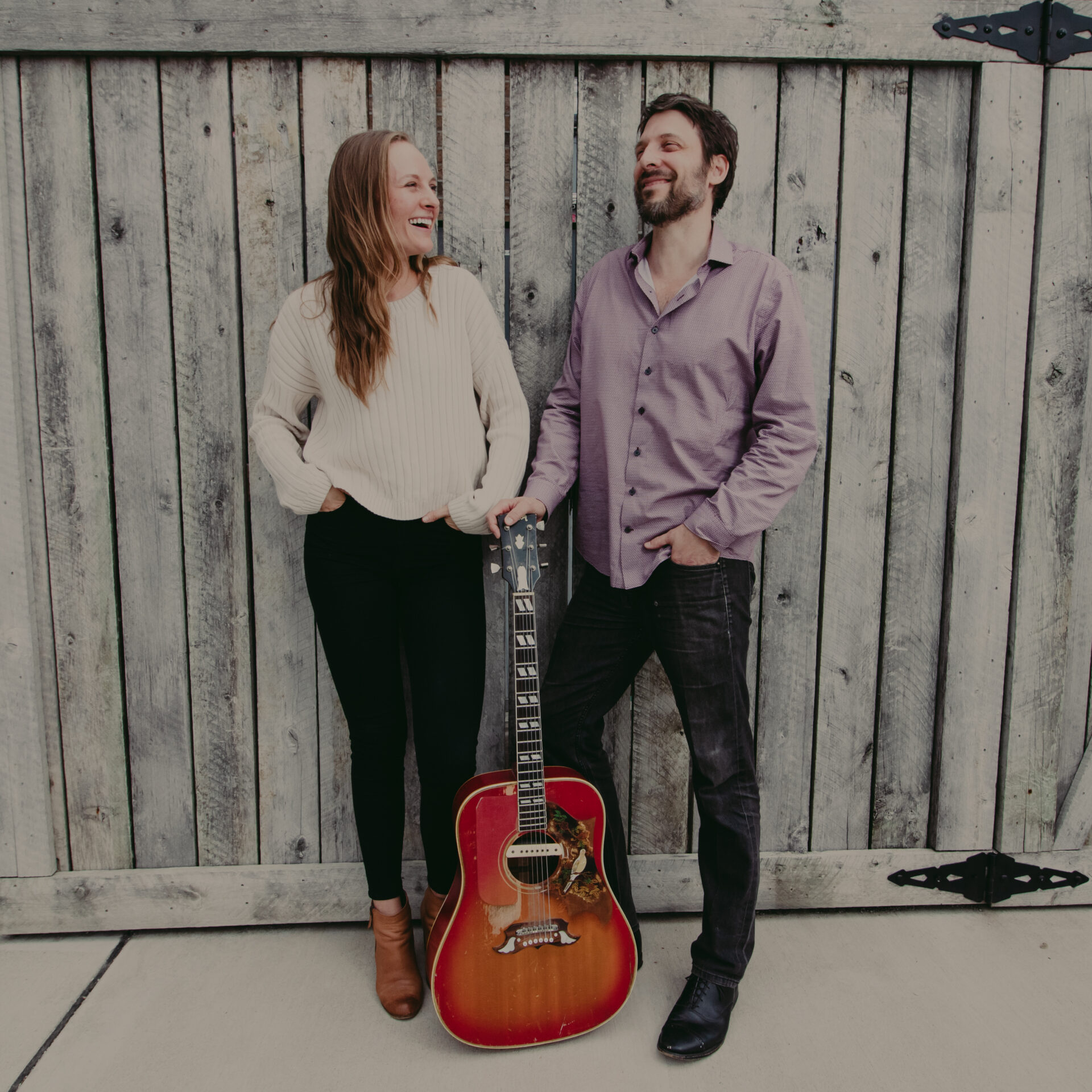 Thrive Companies, A woman and a man stand in front of a rustic wooden gate, smiling at each other. A red acoustic guitar rests upright between them. Apartments in Columbus Ohio