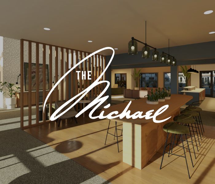 A modern, open-concept lounge with bar stools, wooden accents, and large windows; The Michael at GVX is written in bold script across the image.