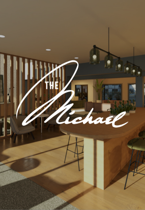 A modern, well-lit interior space with wooden floors, large windows, a long table, and the text The Michael at GVX overlaid in script font.