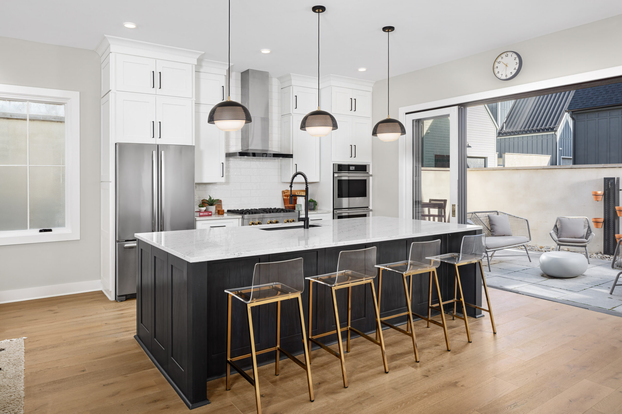 Thrive Companies, Modern kitchen with a large island, four transparent bar stools, stainless steel appliances, pendant lights, and sliding glass doors opening to a patio—perfect for community management gatherings. Apartments in Columbus Ohio