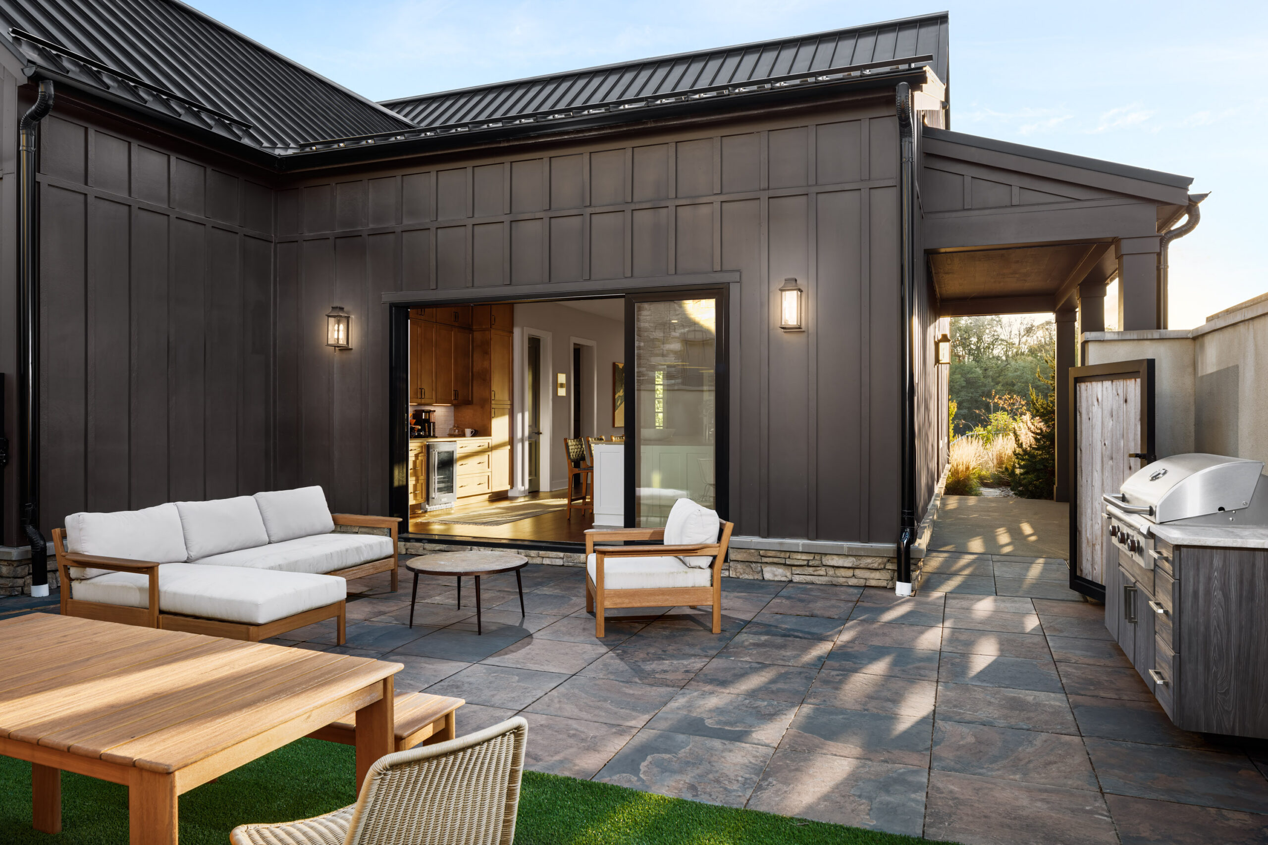 Thrive Companies, Modern patio by Thrive Companies featuring outdoor seating, a dining table, and a grill, adjacent to a dark-paneled house with large sliding glass doors leading to the interior. Apartments in Columbus Ohio