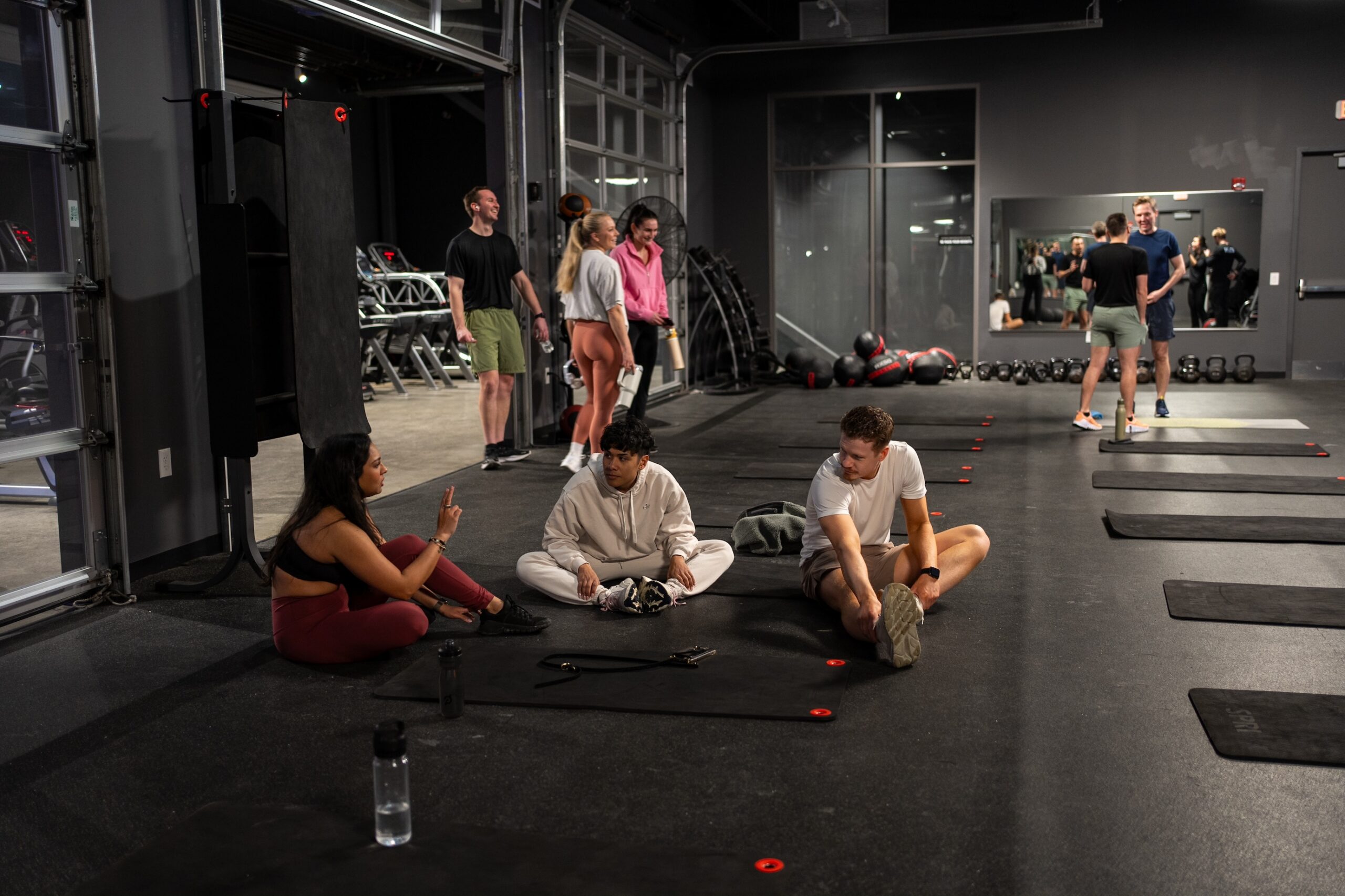 Thrive Companies, Several people are in a gym; three sit and talk on exercise mats in the foreground, while others stand or walk around in the background. Apartments in Columbus Ohio