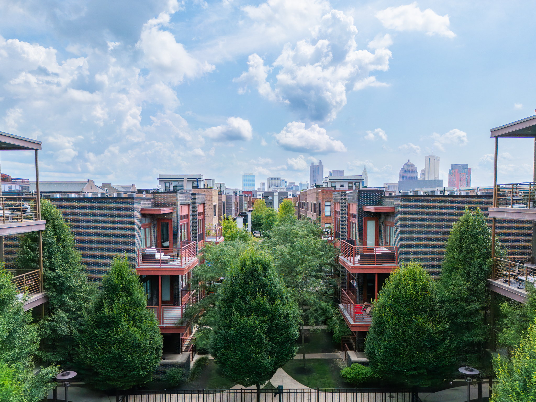 Thrive Companies, View of an urban residential complex by Thrive Companies, featuring modern brick buildings, green trees in the courtyard, and a city skyline in the background under a partly cloudy sky. Apartments in Columbus Ohio