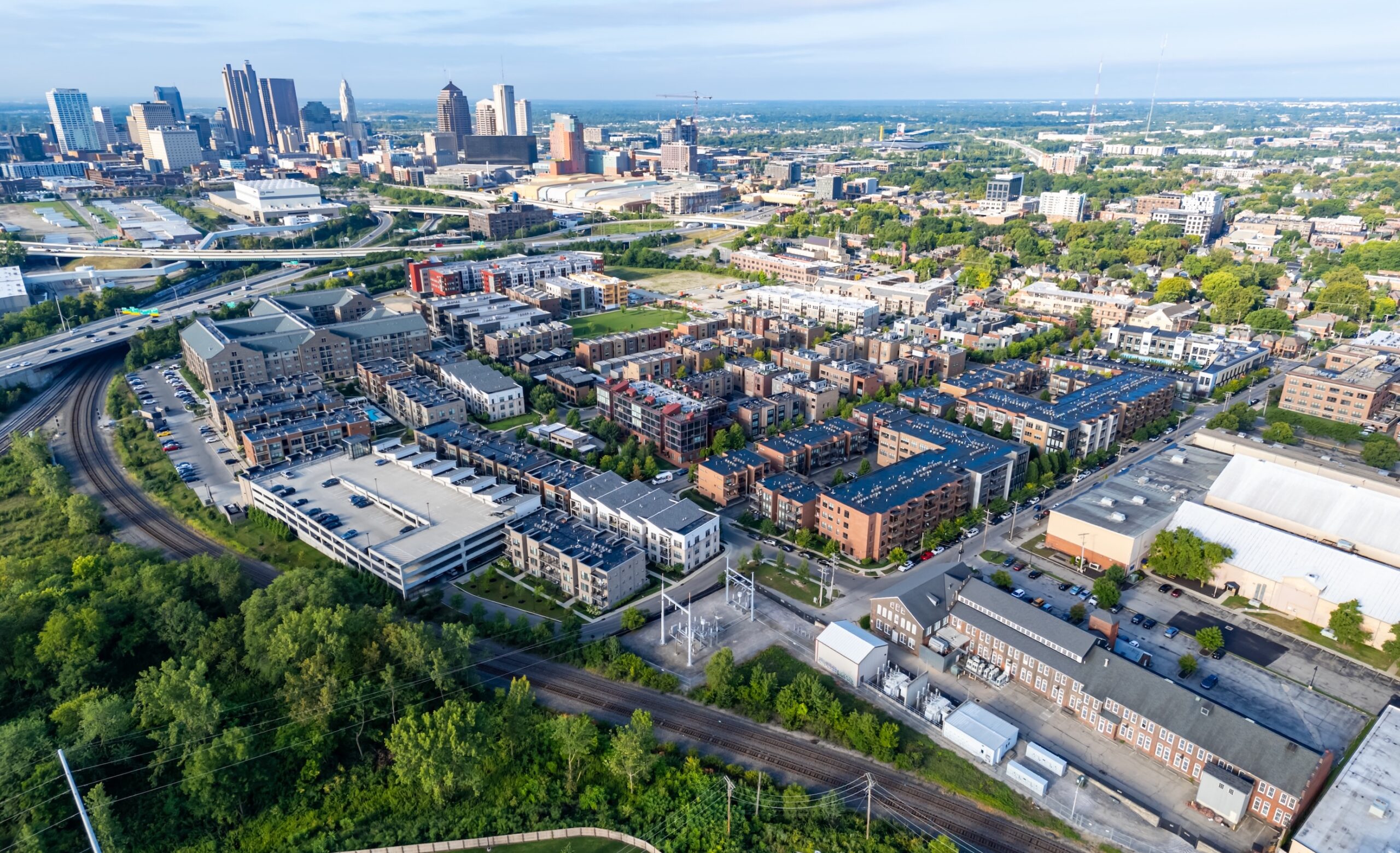 Thrive Companies, Aerial view of a cityscape featuring downtown buildings, residential complexes, a parking garage, train tracks, and green spaces on a clear day. Apartments in Columbus Ohio