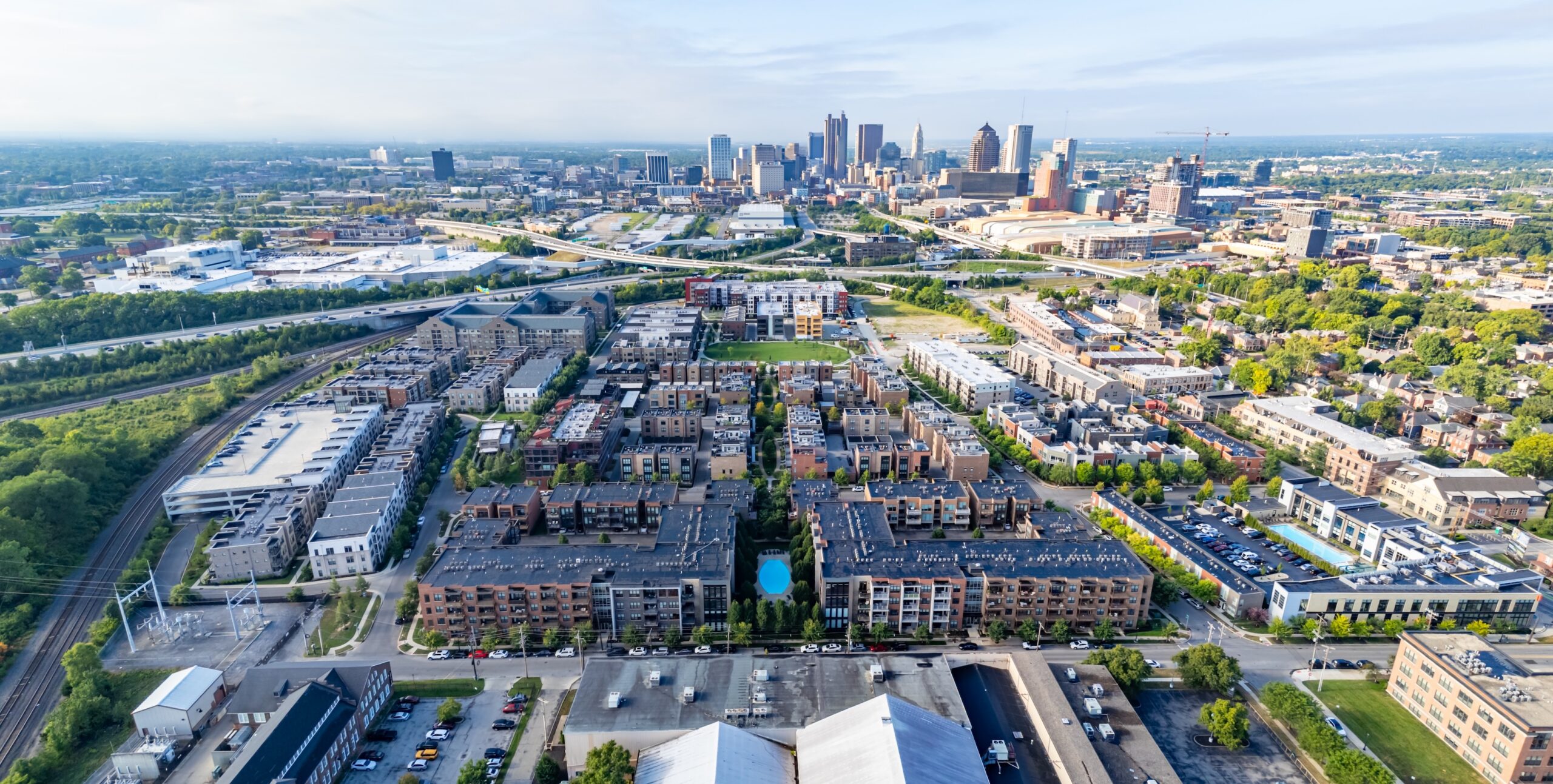 Thrive Companies, Aerial view of a residential neighborhood with apartment buildings and green spaces, with a city skyline in the background under a partly cloudy sky. Apartments in Columbus Ohio