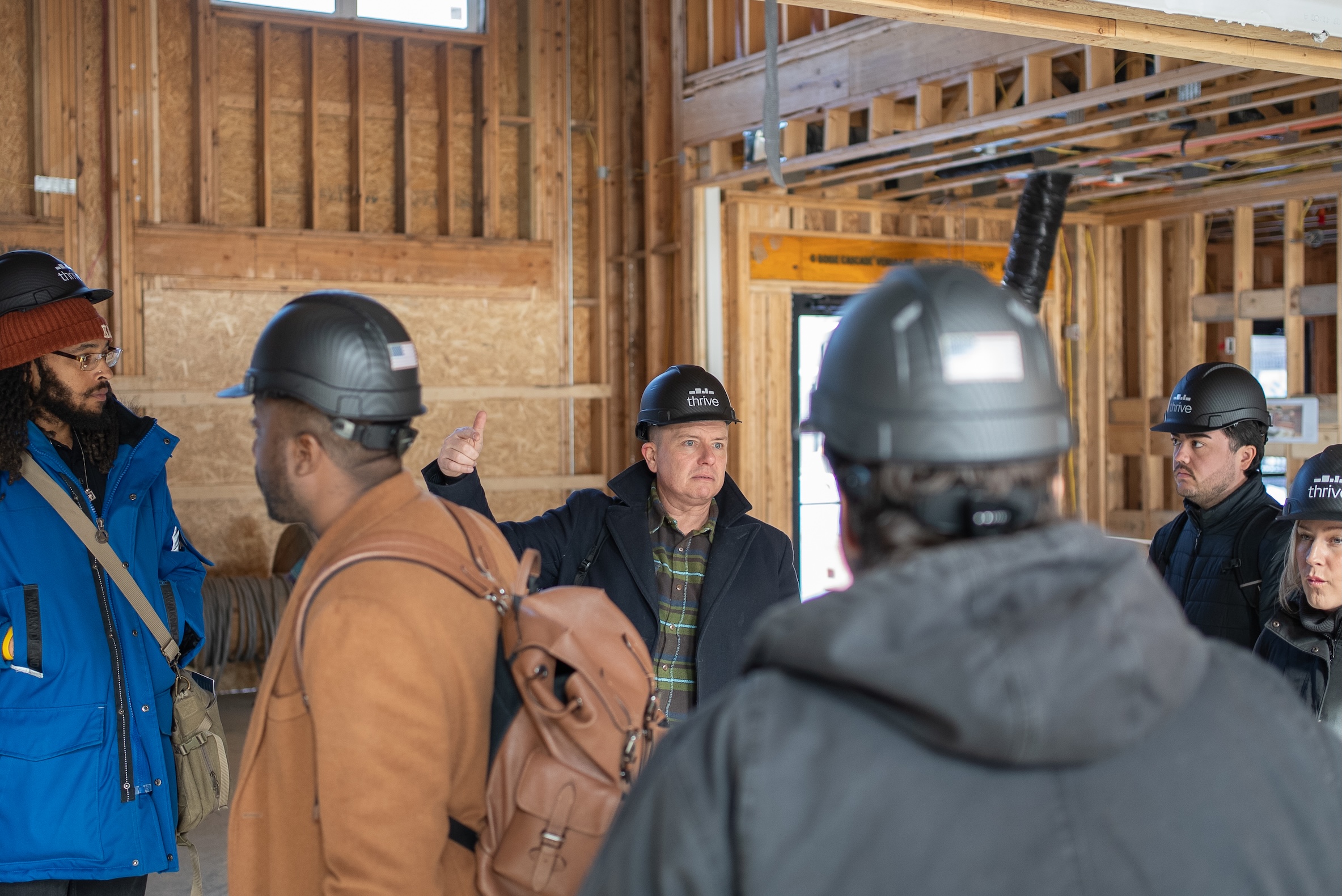Thrive Companies, A group of people wearing hard hats have a discussion about community management inside a building under construction with exposed wooden framing. Apartments in Columbus Ohio