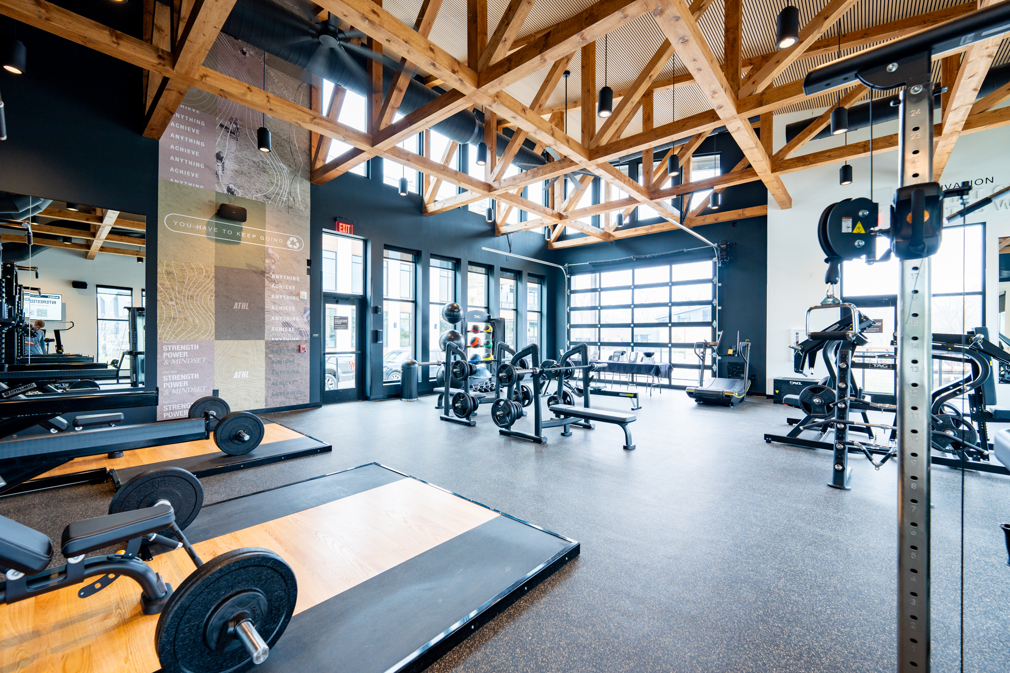 Thrive Companies, A well-lit modern gym with weightlifting platforms, free weights, cardio machines, large windows, and exposed wooden ceiling beams. Apartments in Columbus Ohio