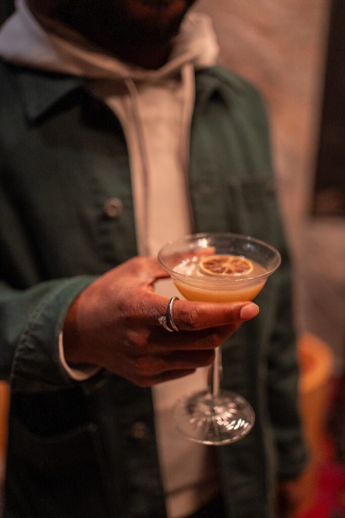 Thrive Companies, A person wearing a dark green jacket and white hoodie holds a cocktail glass with a dried citrus garnish, capturing the stylish urban vibe inspired by Thrive Companies. Apartments in Columbus Ohio