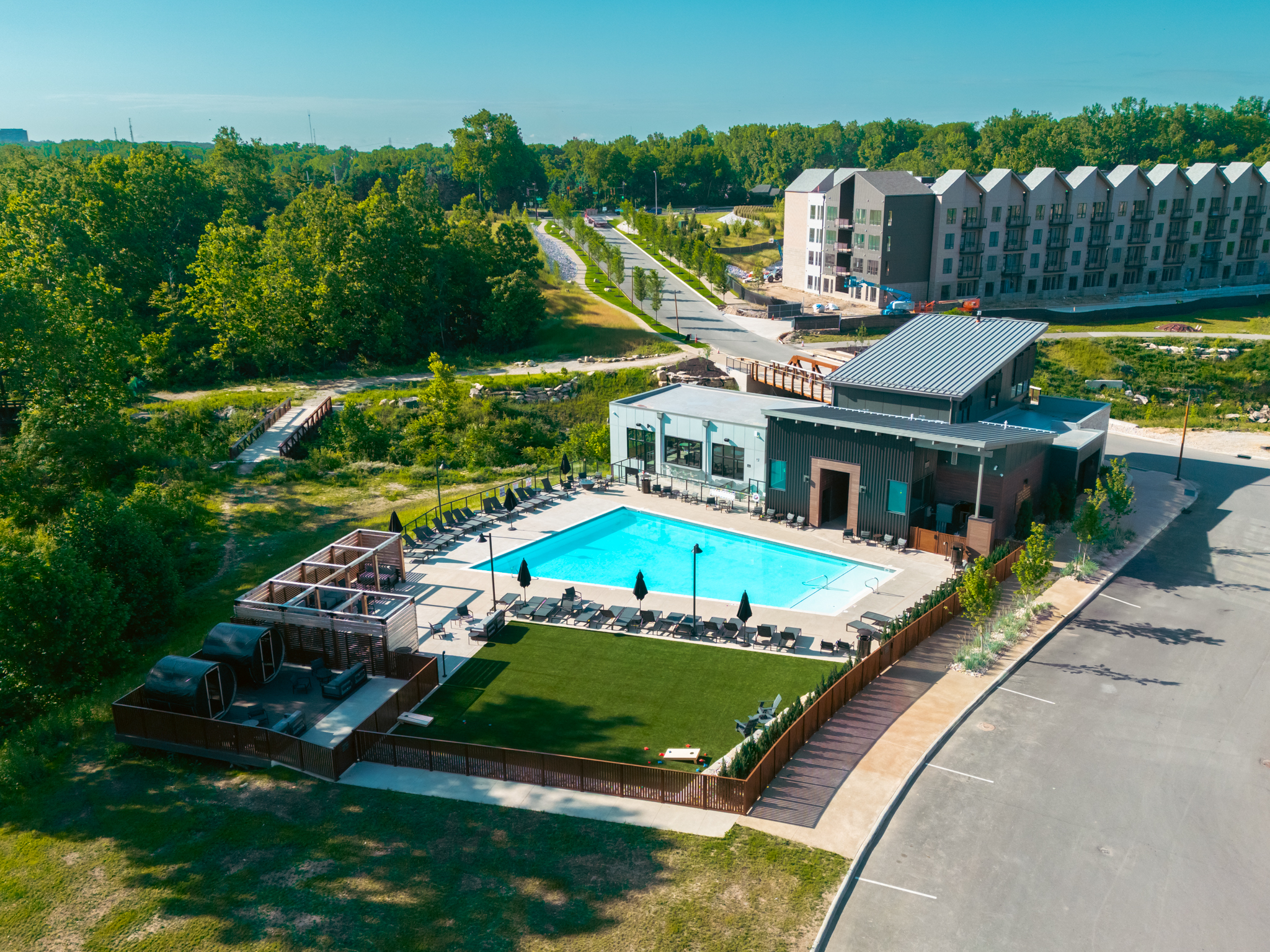Thrive Companies, Aerial view of a modern outdoor pool area by Thrive Companies, featuring lounge chairs, cabanas, and a building, all surrounded by lush greenery and stylish apartment buildings. Apartments in Columbus Ohio